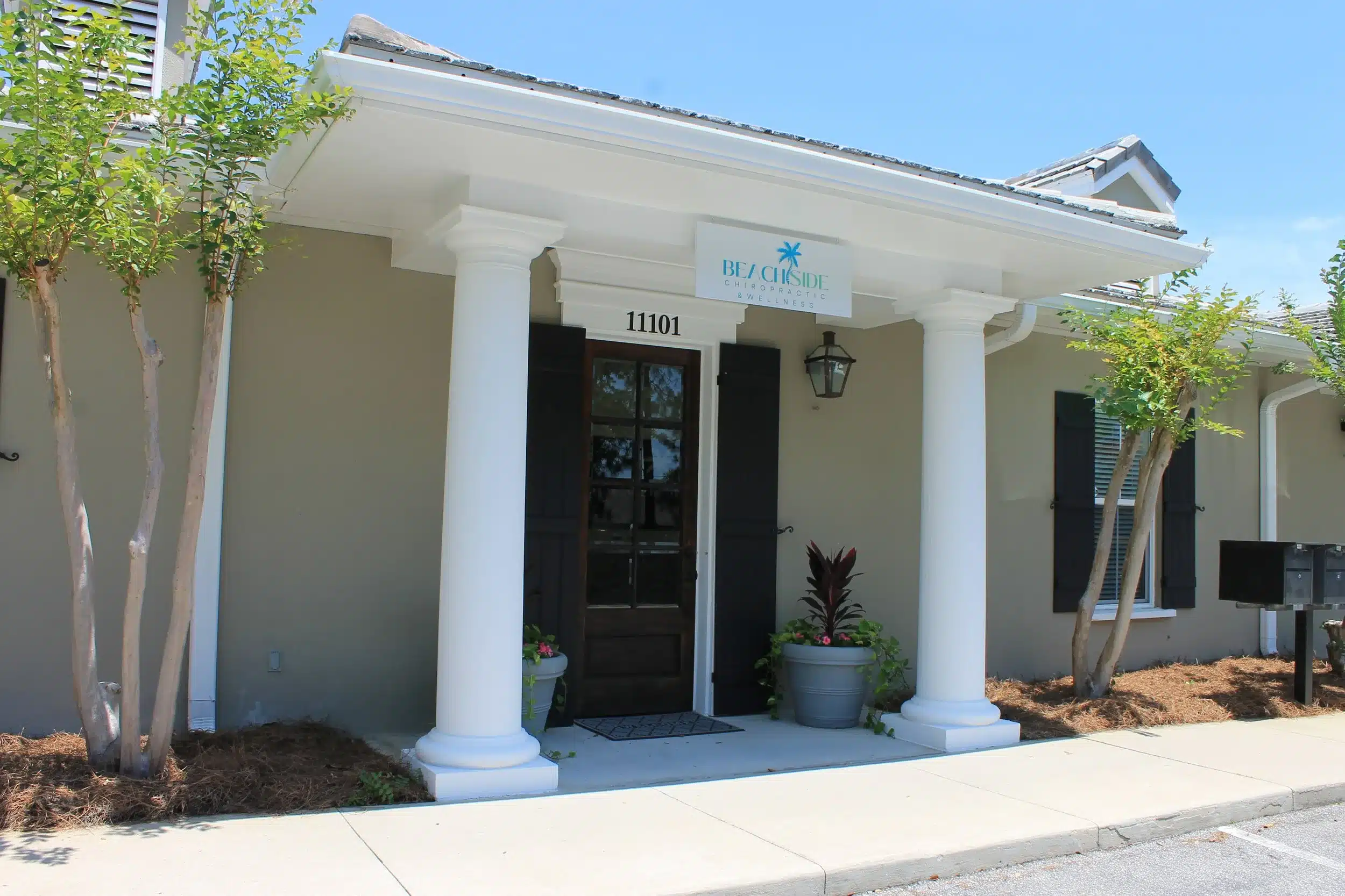 The front entrance of Beachside Chiropractic & Wellness, featuring white columns, potted plants, and the clinic's sign above the door, located in Destin, Florida.